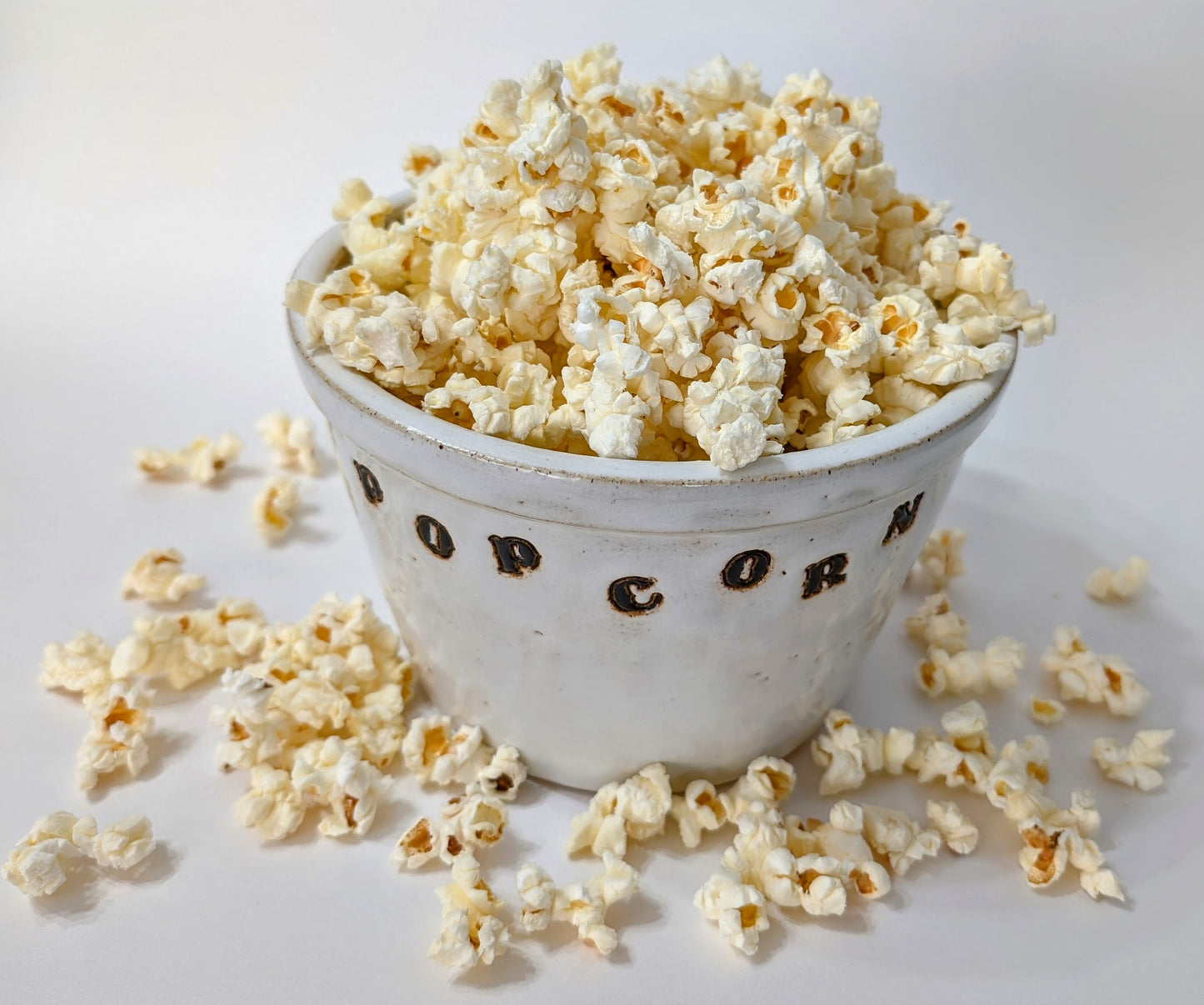 A white ceramic bowl filled with popped popcorn kernels 